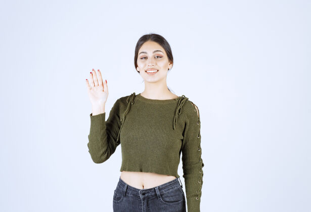 女人一个穿着绿色毛衣微笑的年轻女子挥舞着一只手挥手摆姿势微笑