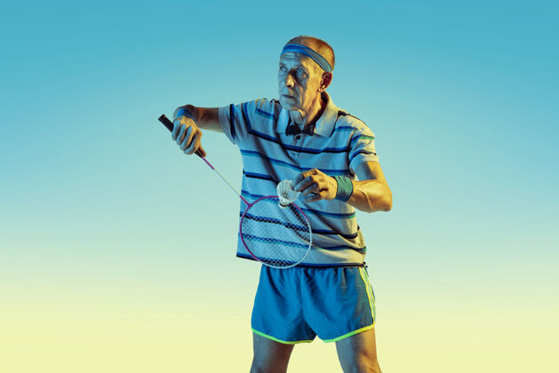 教练穿运动服的高级男士在梯度背景下打羽毛球 霓虹灯身材魁梧的白人男模保持活跃运动 活动 运动 健康 自信的概念活动运动员男子