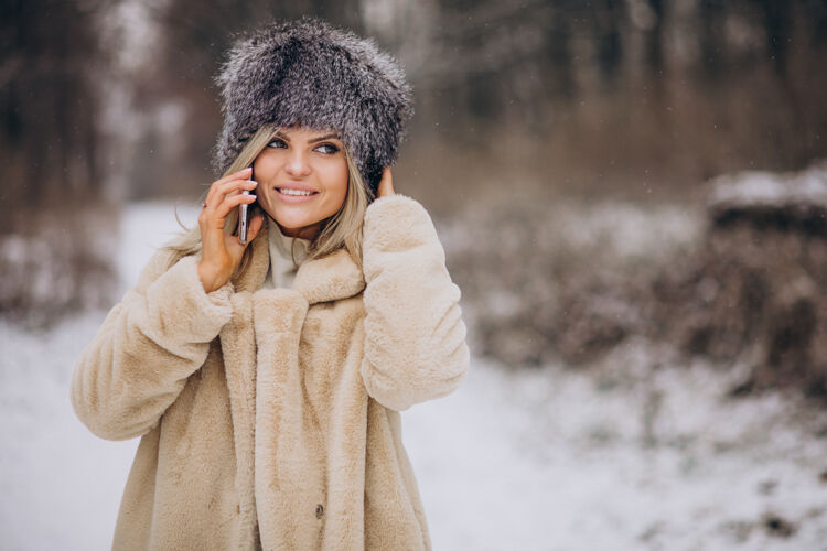 移动穿着冬衣的女人走在满是雪的公园里打电话自然树女孩