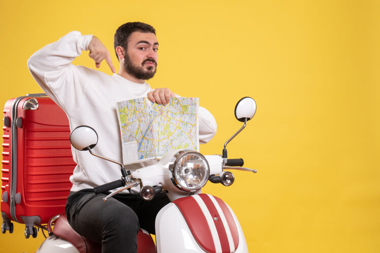 训练旅行的概念与惊讶的男子坐在摩托车上的手提箱 它指向黄色地图旅行男地图
