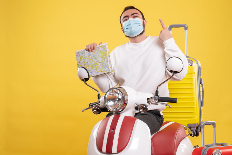 站立旅行概念的俯视图 戴着医用面罩的自信的家伙站在摩托车旁边 黄色手提箱放在上面 手里拿着地图男性地图顶部