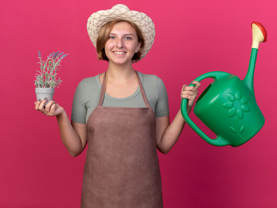 花园微笑着的年轻的斯拉夫女园丁戴着园艺帽 手里拿着浇水罐 花盆里放着鲜花举行穿女性