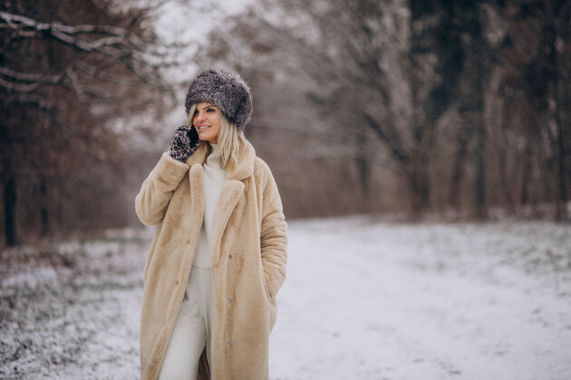 森林穿着冬衣的女人走在满是雪的公园里打电话女孩移动帽子