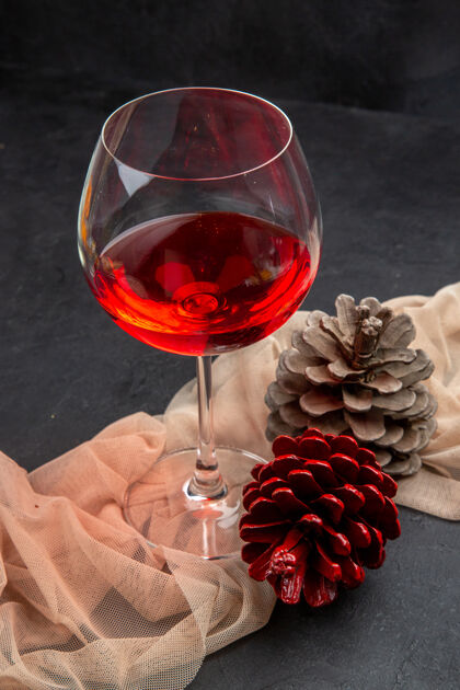 酒杯前视图美味的红酒在玻璃高脚杯毛巾和针叶树锥在黑暗的背景酒精深色玻璃杯