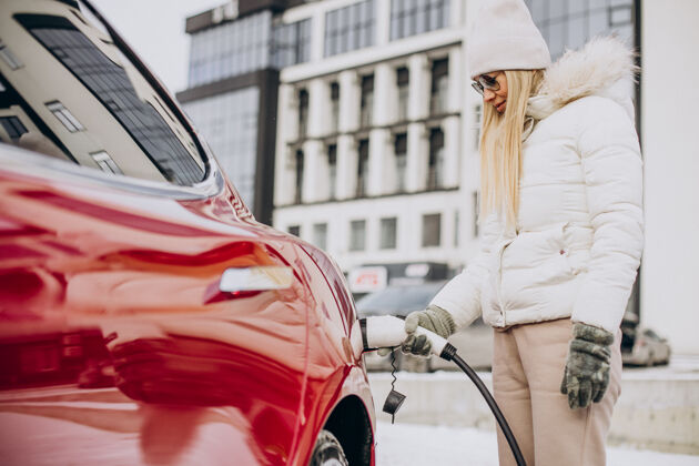 寒冷女人充电红色电动车 在冬天的时候太阳镜停车汽车