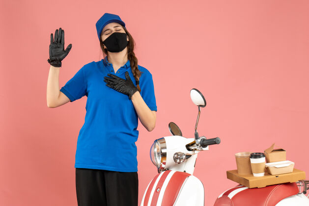 手套俯视图：戴着医用面罩手套的信使女孩站在摩托车旁 车上放着咖啡蛋糕 在柔和的桃色背景下做梦穿人物粉彩