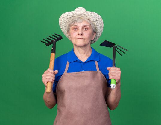 老人自信的上了年纪的女园丁戴着园艺帽拿着耙子和锄头耙子帽子信心耙