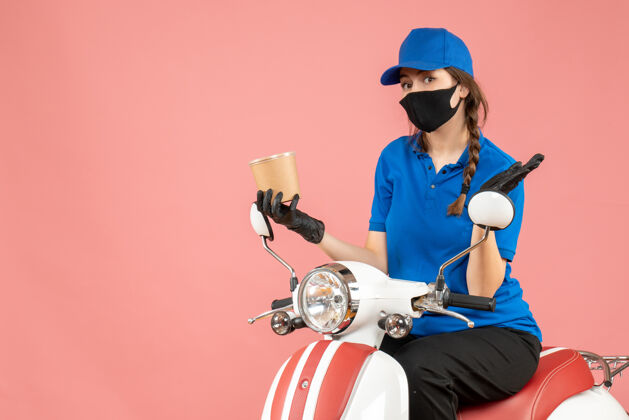 惊喜俯视图惊讶的女快递员戴着医用口罩和手套坐在滑板车上传递粉彩桃的订单订单视图面具
