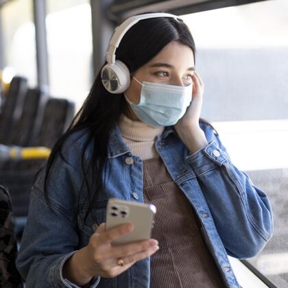 公共汽车带着面具和耳机旅行的女人面罩旅行汽车
