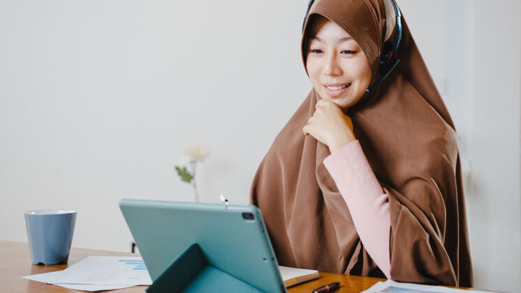 商务女性女士戴着耳机使用数字平板电脑在家里厨房工作时 通过视频会议与同事谈论销售报告耳机远程伊斯兰