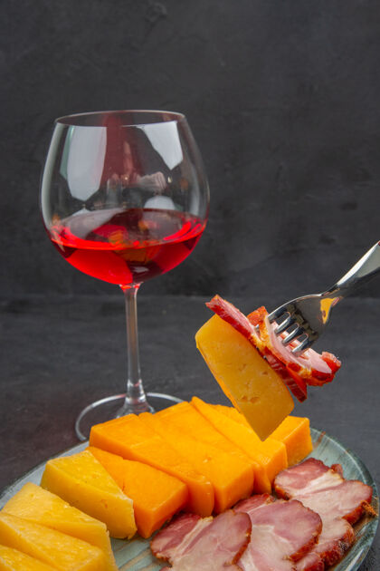 深色用叉子拉手的特写镜头蓝色盘子里美味的香肠和奶酪片 黑色背景上的红玫瑰切片奶酪新鲜