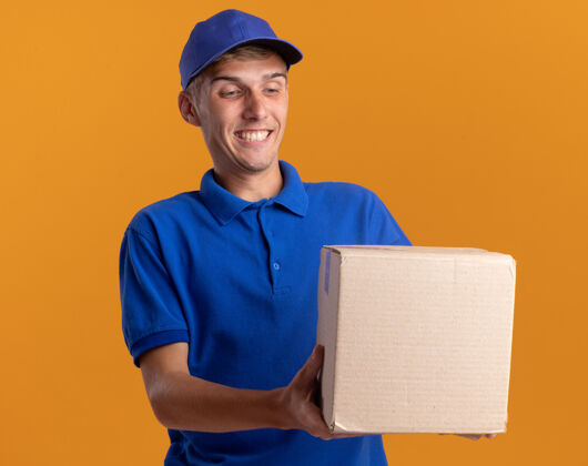金发微笑着的年轻金发送货员抱着并看着cardbox送货年轻微笑