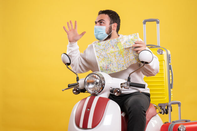 坐着旅行的概念与自信的家伙在医疗面具坐在摩托车上 黄色的手提箱上黄色旅行医疗