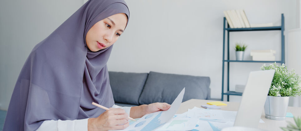 阿拉伯语美丽的亚洲女士戴着头巾 穿着休闲服 在家里的客厅里使用笔记本电脑文化自由职业者印度人