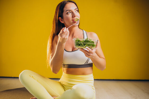 运动装在黄色背景上吃沙拉的女人女运动员素食主义者欧洲