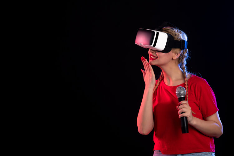 虚拟现实年轻女性在黑暗的墙上玩虚拟现实和用麦克风唱歌的画像黑色游戏麦克风