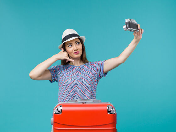 航行度假的女人拿着相机在蓝色上拍照行李持有旅行