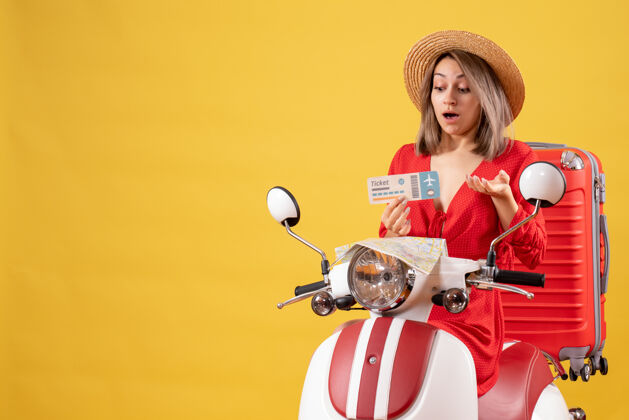 时尚穿着红衣服的年轻女士惊讶地看着轻便摩托车上的车票成人表情惊喜小姐
