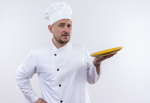 厨艺自信的年轻帅哥厨师穿着厨师制服把盘子放在孤零零的白墙上制服厨师自信