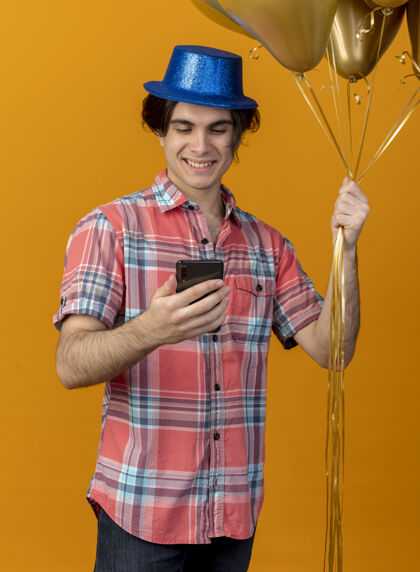 橙色高加索帅哥戴着蓝色派对帽 手里拿着氦气球 看着手机拿着请帅哥