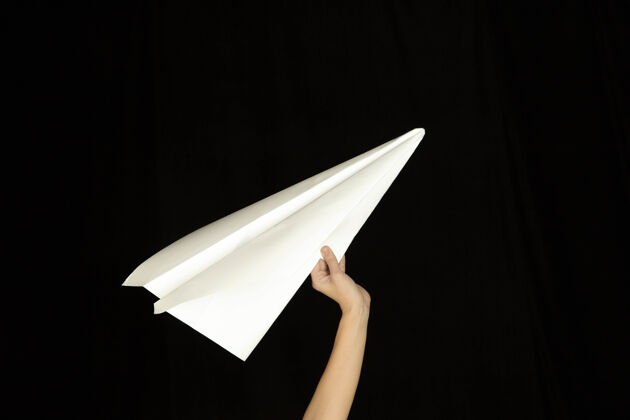 媒体手持黑色背景纸飞机标志或信息的手广告纸发送