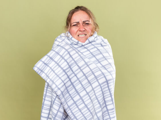 不健康不健康的妇女裹着毯子 感觉很可怕 患流感和感冒 高烧站在绿色的墙壁上毛毯感觉女人