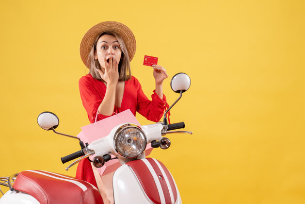 信贷一个穿着红色衣服 手持购物袋和信用卡 坐在轻便摩托车上的惊讶女人摩托车设备购物