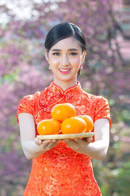 展示美丽的亚洲女人开心地微笑着 手里拿着粉红背景的新鲜橘子过年空白红色微笑