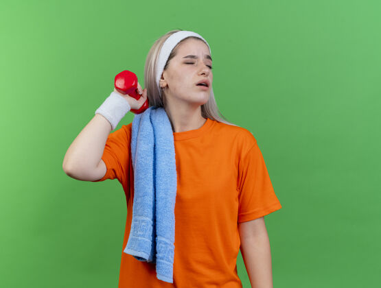空间年轻的白人运动女孩戴着背带 头上戴着头带 肩上戴着毛巾 手上拿着哑铃哑铃肩膀毛巾