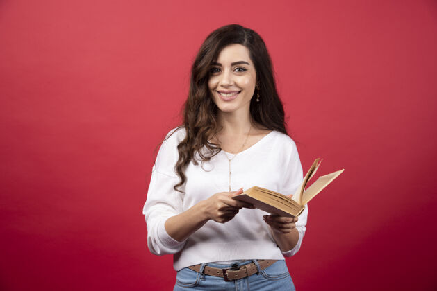 女人站在红色背景上看书的女人高质量的照片手持年轻人
