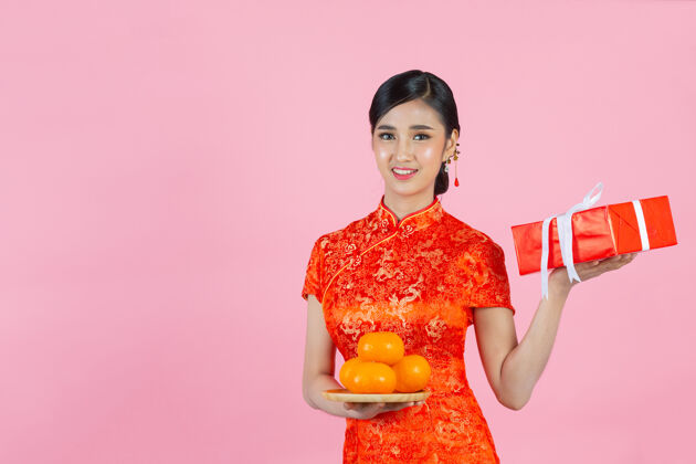 红色美丽的亚洲女人开心地微笑着 手里拿着粉红背景的新鲜橘子过年女士礼品中文
