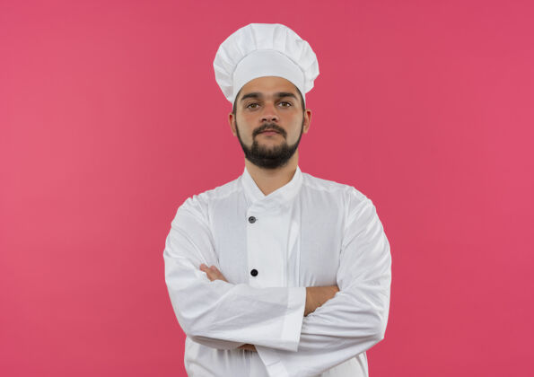 站立自信的年轻男性厨师身着厨师制服 以封闭的姿势站在粉色墙壁上 有复制空间制服厨师烹饪