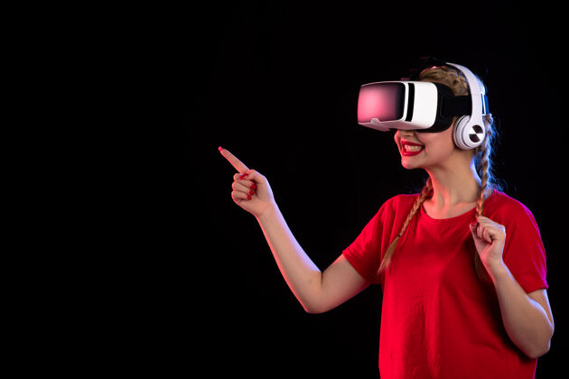 女士戴着耳机在黑暗的墙上玩虚拟现实的年轻女士的正视图耳机成人播放