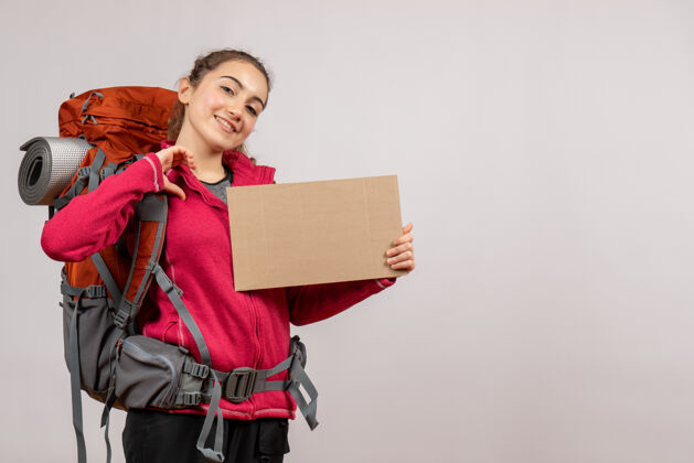 女士带着微笑的年轻旅行者 背着大背包 手里拿着灰色的纸板背包灰色纸板