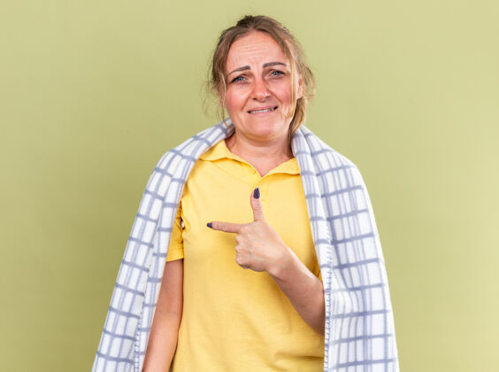 手指不健康的妇女裹着毛毯 感觉不舒服 患流感和感冒 发烧 食指指向绿墙那边发烧壁板目录