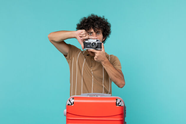 红色带着大红色手提箱的度假男人用蓝色的相机拍照视图手提箱照片