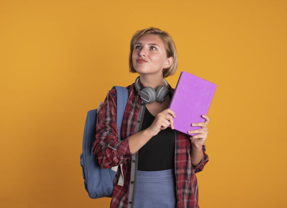 背包印象深刻的年轻斯拉夫女学生戴着耳机背着书包拿着书和笔记本看着身边橙色学生壁板
