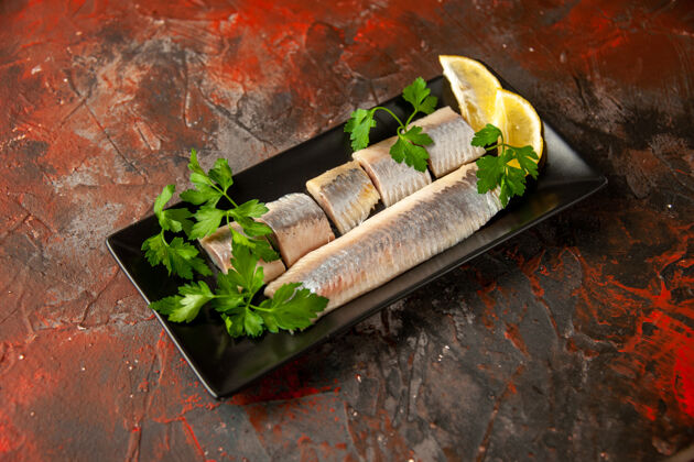 香草前视图新鲜鱼片与绿色和柠檬片在黑色平底锅内的黑色零食肉类食品瓶子叶子块