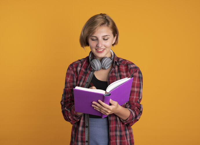 空间微笑的年轻斯拉夫女学生戴着耳机 背着书包 用笔在书上写字女孩微笑穿着