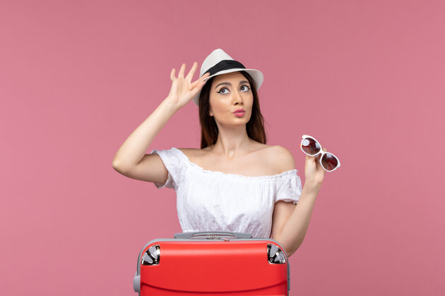年轻女子正面图：年轻女子手持帽子准备度假 背景为浅粉色 远航出海旅行帽子成人