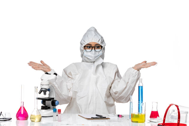 面罩正面图身穿特殊防护服的年轻女化学家坐在白色办公桌上 拿着解决方案病毒实验室covid健康化学实验室特殊化学