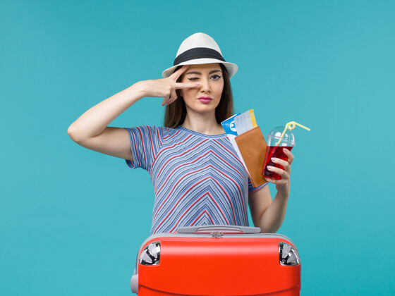 成人前景度假中的女人拿着果汁和浅蓝色背景上的机票远航旅程中的女性海上避暑飞机休闲航程持有