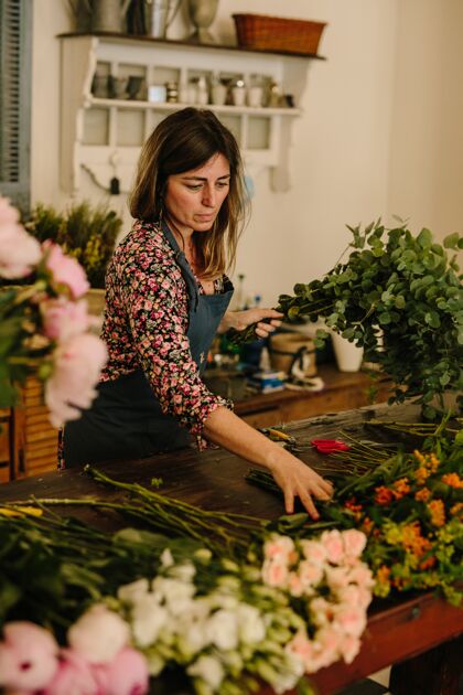 女人欧洲女花匠与绿色围裙在花卉设计工作室插花工作安排花园