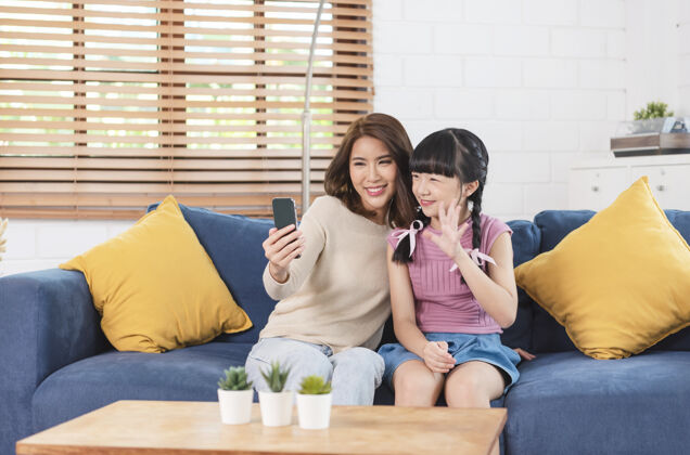 亚洲快乐的亚洲家庭在家客厅的沙发上用智能手机合影学习关系微笑