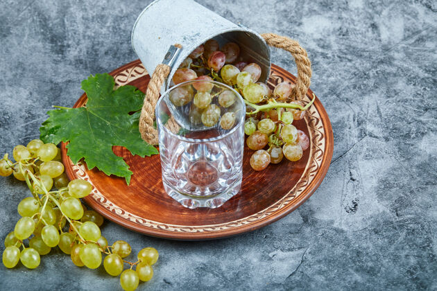 串陶瓷盘上放着一小桶葡萄 大理石上放着一个玻璃杯果汁绿色食物