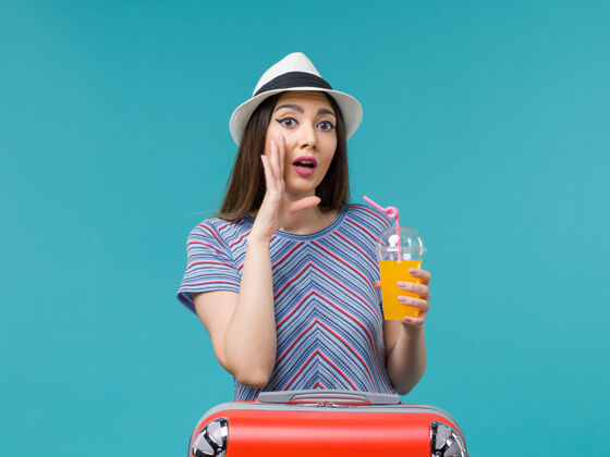 女性前视图度假妇女与她的红色袋子举行浅蓝色背景她的果汁旅行度假女性持有旅行成人