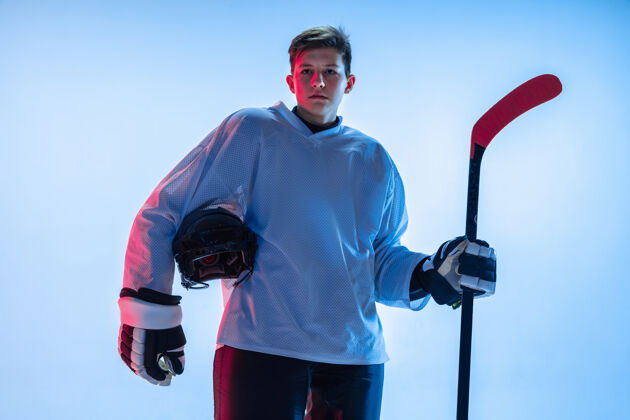 活跃年轻的男性冰球运动员在霓虹灯下用棍子粘在白墙上青少年团队合作头盔