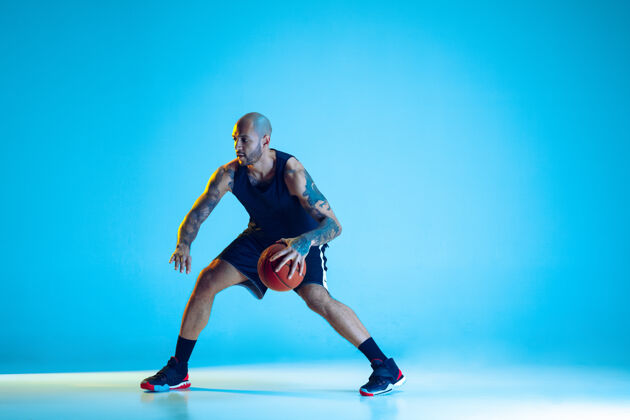 帅哥年轻的篮球队员穿着运动服训练 在行动中练习 在霓虹灯下隔离在蓝色的墙上版权空间篮子扣篮