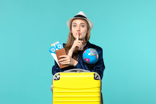 年轻女子正面图年轻女子拿着机票和地球仪在蓝色背景的飞机上海上度假旅行肖像航程举行