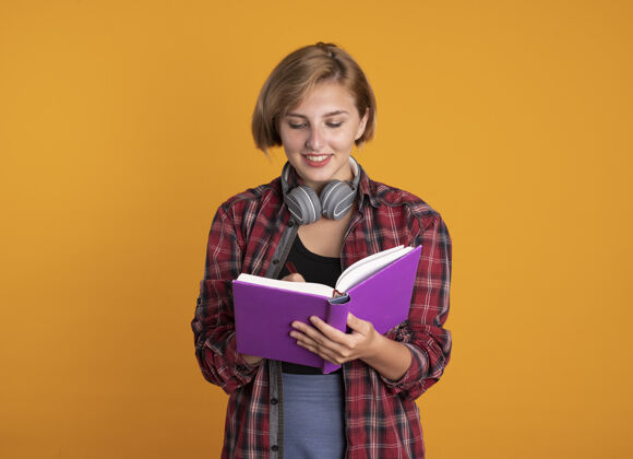 空间微笑的年轻斯拉夫女学生戴着耳机 背着书包 用笔在书上写字女孩微笑穿着